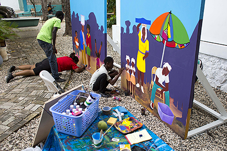 In this May 25, 2016 photo, Haitian visual artist Tessa Mars stretches out on a concrete path to correct a detail on the bottom of a student's oil painting, at the resurrected Centre d’Art or Art Center in Port-au-Prince, Haiti. Mars is helping the students who hope to enter their work in a best depictions of daily life in a democracy compeition. (AP Photo/Dieu Nalio Chery)